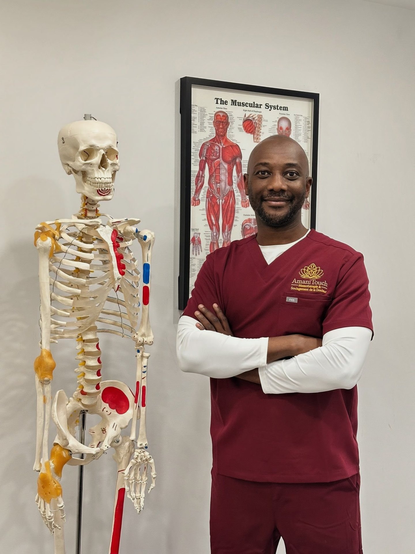 Ofure Osifo, massothérapeute agréé, à côté d'un squelette anatomique et d'une affiche du système musculaire