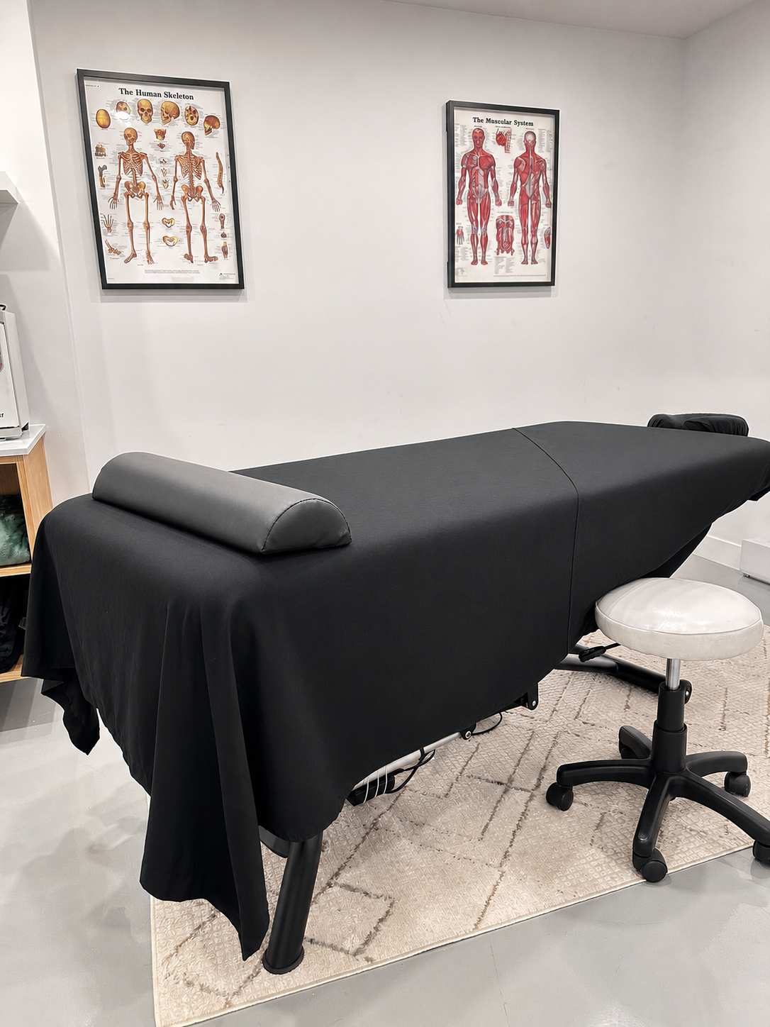 Salle de traitement AmaniTouch avec table de massage et affiches anatomiques du squelette humain et du système musculaire