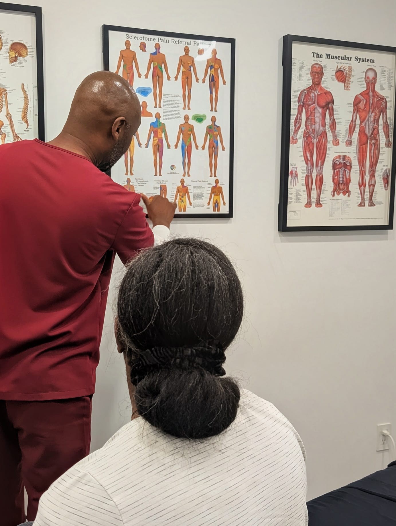 AmaniTouch massage therapist explaining anatomical charts to a seated client during a consultation.